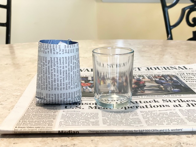 newspaper pot for seed starting and glass votive holder on newspaper page