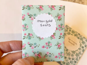 diy seed packet made from blue scrapbook paper with pink roses, and labeled as marigold seeds